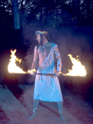 Zeus (Julian Allescher) mit langem Feuerstab in dominanter selbstsicherer Pose.